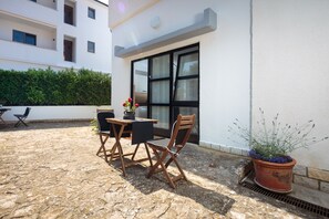Un espacio al aire libre con mesa y sillas, una planta en maceta y la entrada de un edificio.
