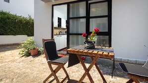 Une terrasse extérieure avec une table en bois, deux chaises et un pot de fleurs contenant des fleurs rouges.