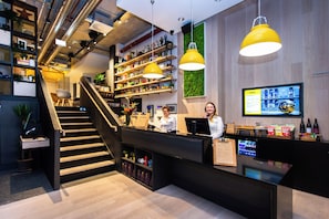 Un hall d’hôtel moderne avec un comptoir d’accueil, un escalier en bois et un mur végétal.