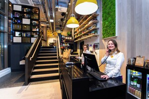Un hall d’hôtel moderne avec un escalier, un comptoir d’accueil et un mur végétal.