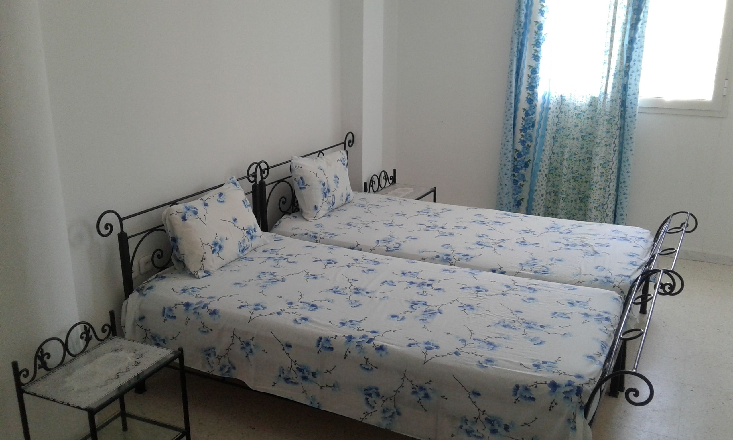 Un lit double avec une couvre-lit à motifs floraux, une table de chevet et une fenêtre avec des rideaux.