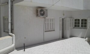 A room with a tiled floor, a white air conditioning unit mounted on the wall, and a window with shutters. - Residence MahdiaSquare (Mahdia)
