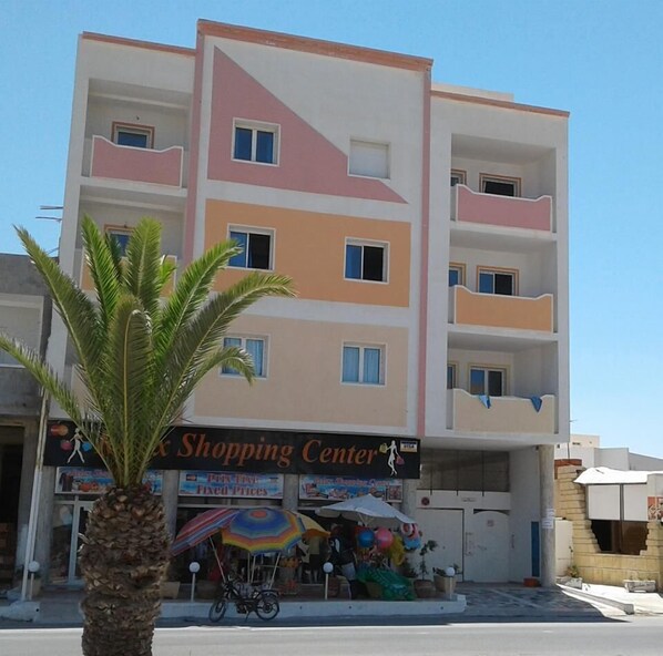A multi-story building with a 'Shopping Center' sign, balconies, and a palm tree in front. - Residence MahdiaSquare (Mahdia)