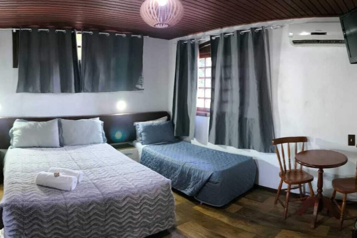 A room with two beds, a small table, two chairs, a TV, and a window with curtains.