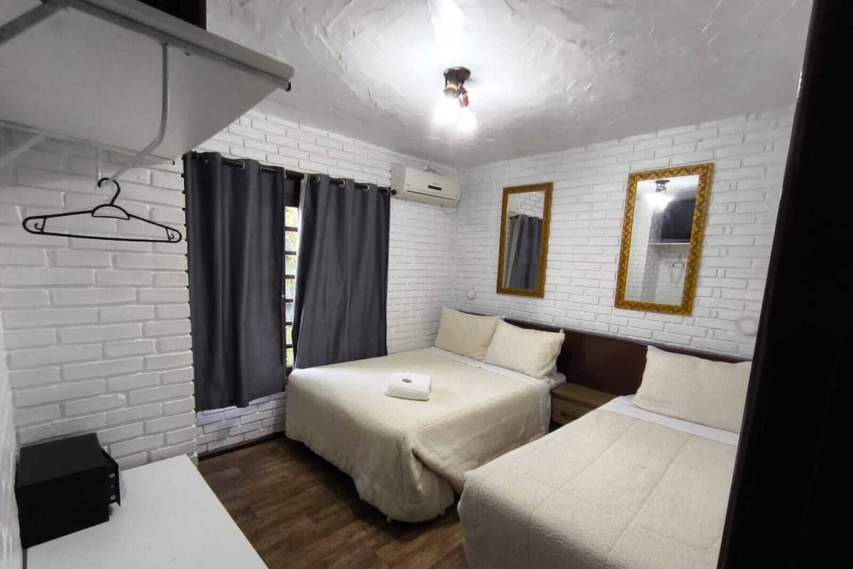 A room with two beds, a white brick wall, a wooden floor, a desk, and a hanging coat rack.