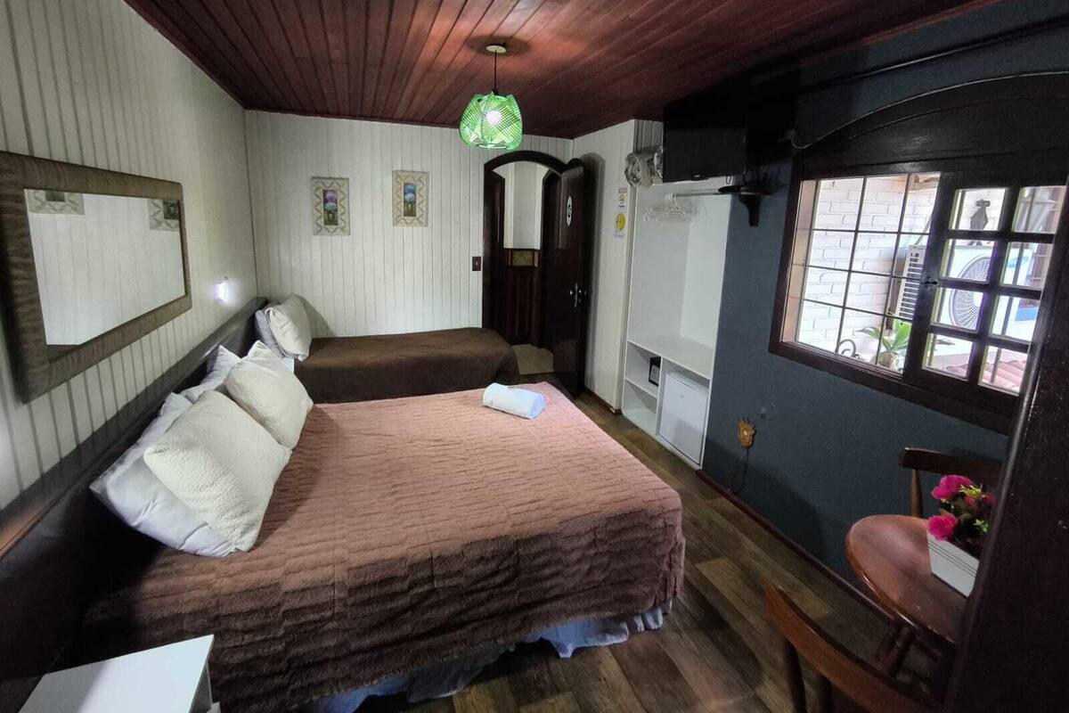 A room with two beds, a wooden ceiling, a window with bars, and a chair with flowers.