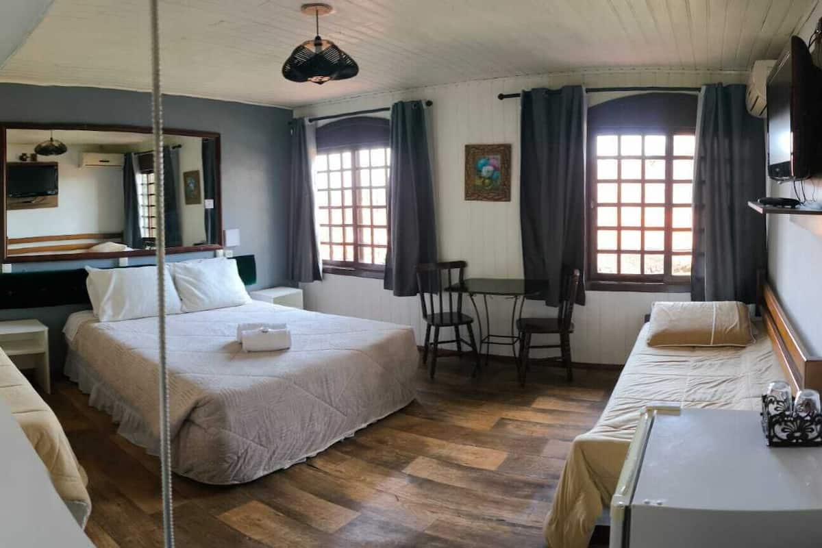 A hotel room with a bed, a desk, a chair, a hanging light, a TV, and a window with curtains.