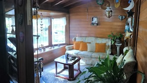 A cozy living room with a wooden ceiling, a sofa with orange cushions, a coffee table, and a large window. - Pousada Casa da Colina (Gramado)