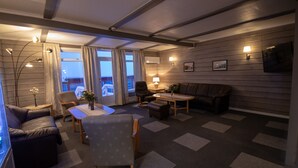 En hyggelig stue med sofa, lænestol og et lille bord. Der er et vindue med gardiner, en lampe og et billede på væggen.