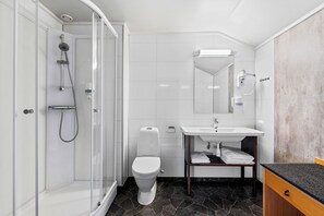 A modern bathroom with a glass-enclosed shower, a white toilet, a sink with a mirror above it, and a dark countertop.