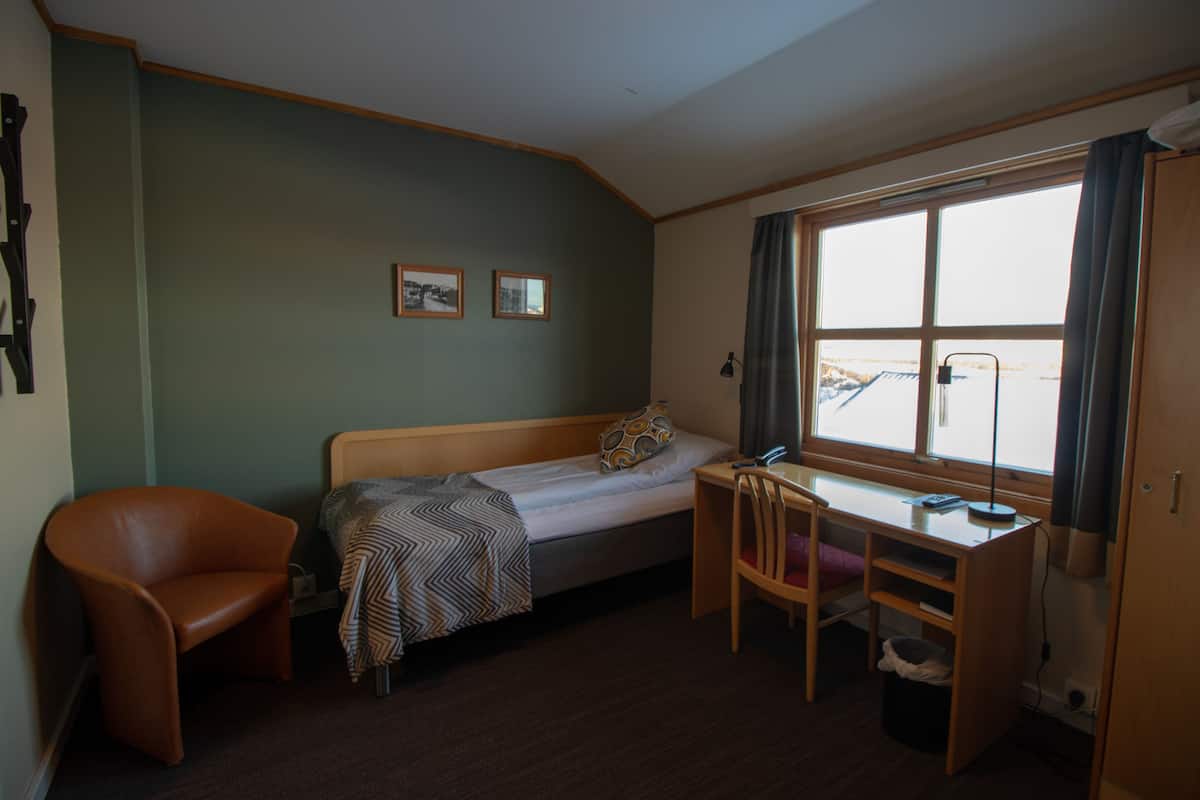A small, compact room with a single bed, a desk, a chair, and a window.