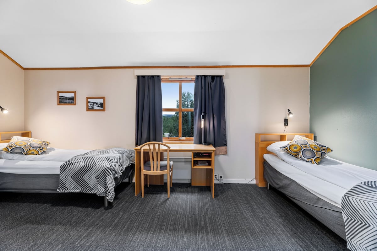 A room with two single beds, a desk, and a chair, with a window and curtains.