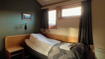 A single bed with a striped blanket, a bedside table, a wall-mounted phone, and a window with curtains.