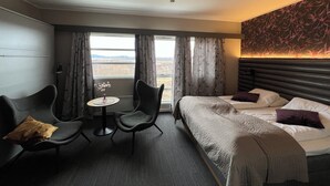 Et hotelværelse med en seng, to stole, et lille bord og udsigt til landskabet.