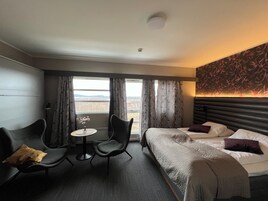A hotel room with a bed, two chairs, a small table, and a view of the landscape.