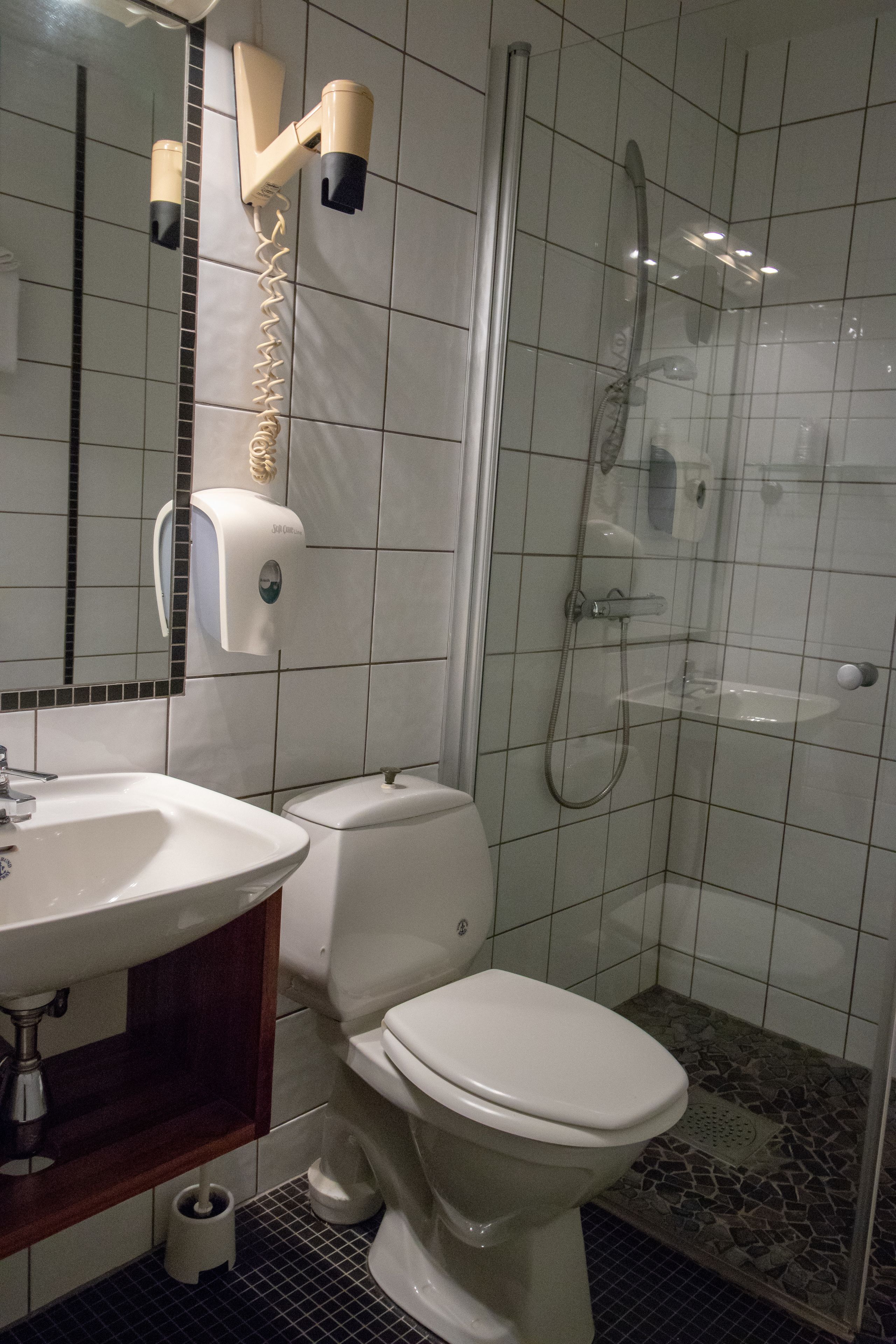 Un baño con inodoro, lavamanos y cabina de ducha con mampara de vidrio.