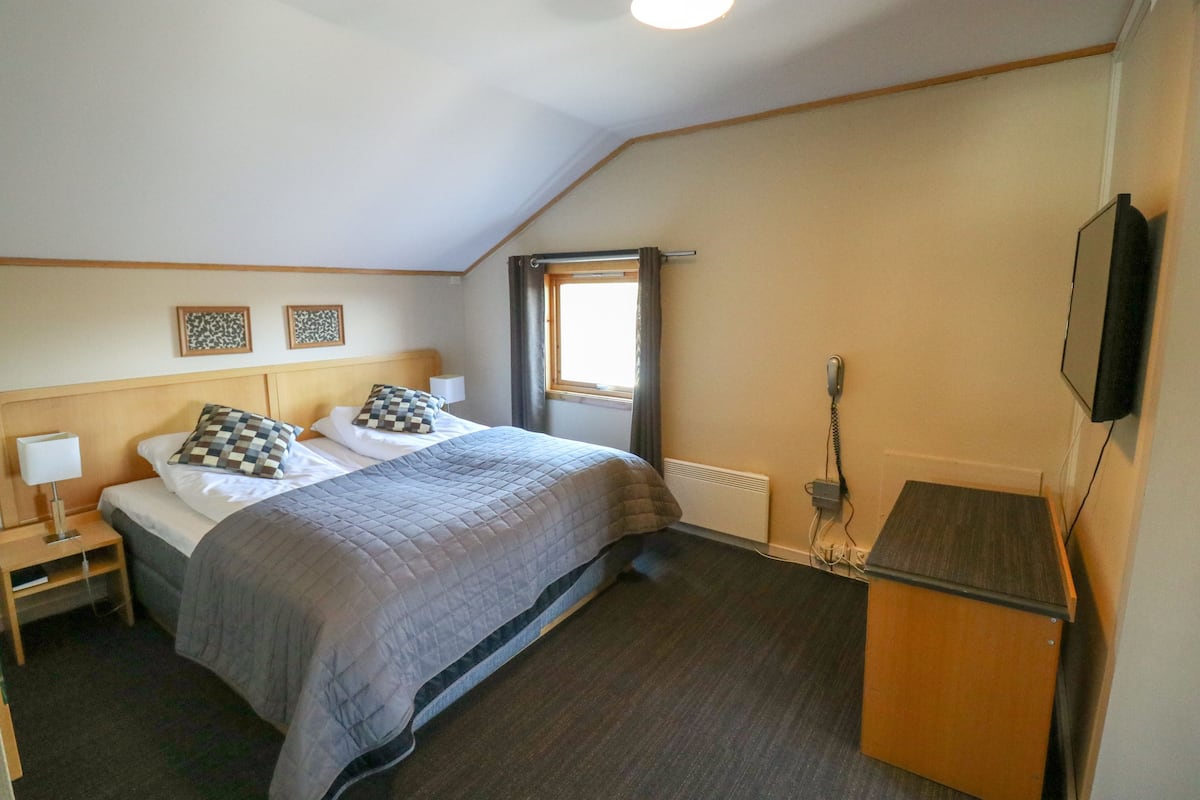 A bedroom with a bed, bedside tables, a TV, and a window.
