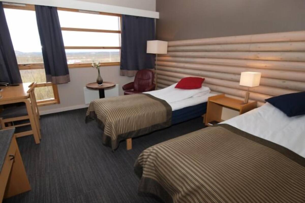 A hotel room with two beds, a desk, a chair, a small table, and a window with curtains.