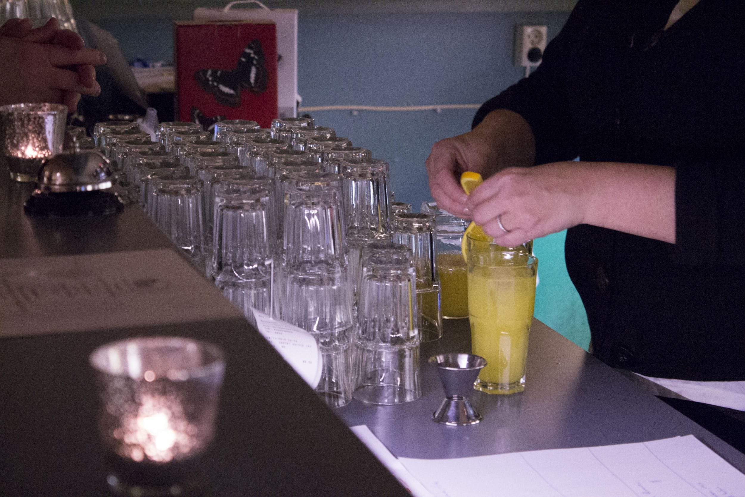 A bar area with multiple glasses lined up and a person squeezing a lemon into a drink.