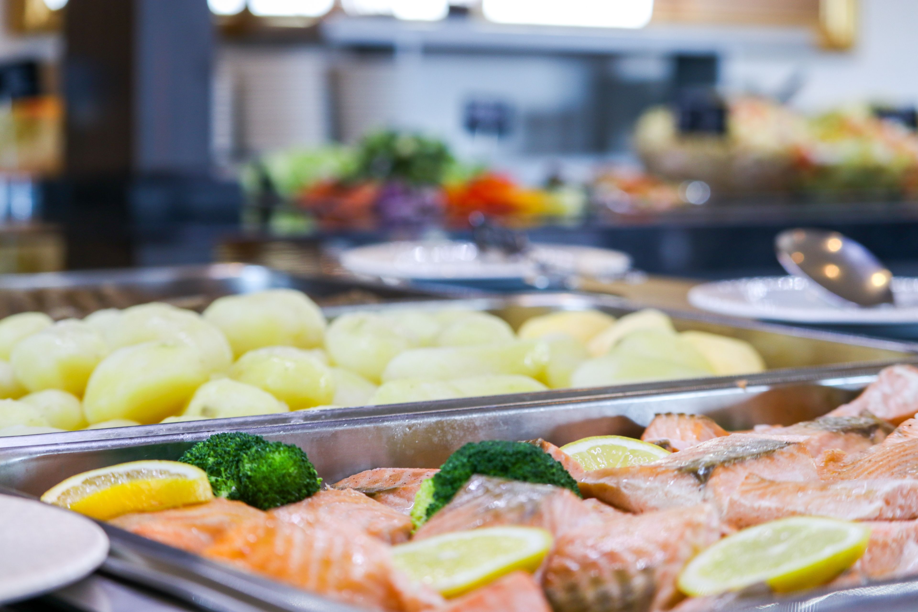 A buffet with salmon, potatoes, broccoli, and lemon slices.