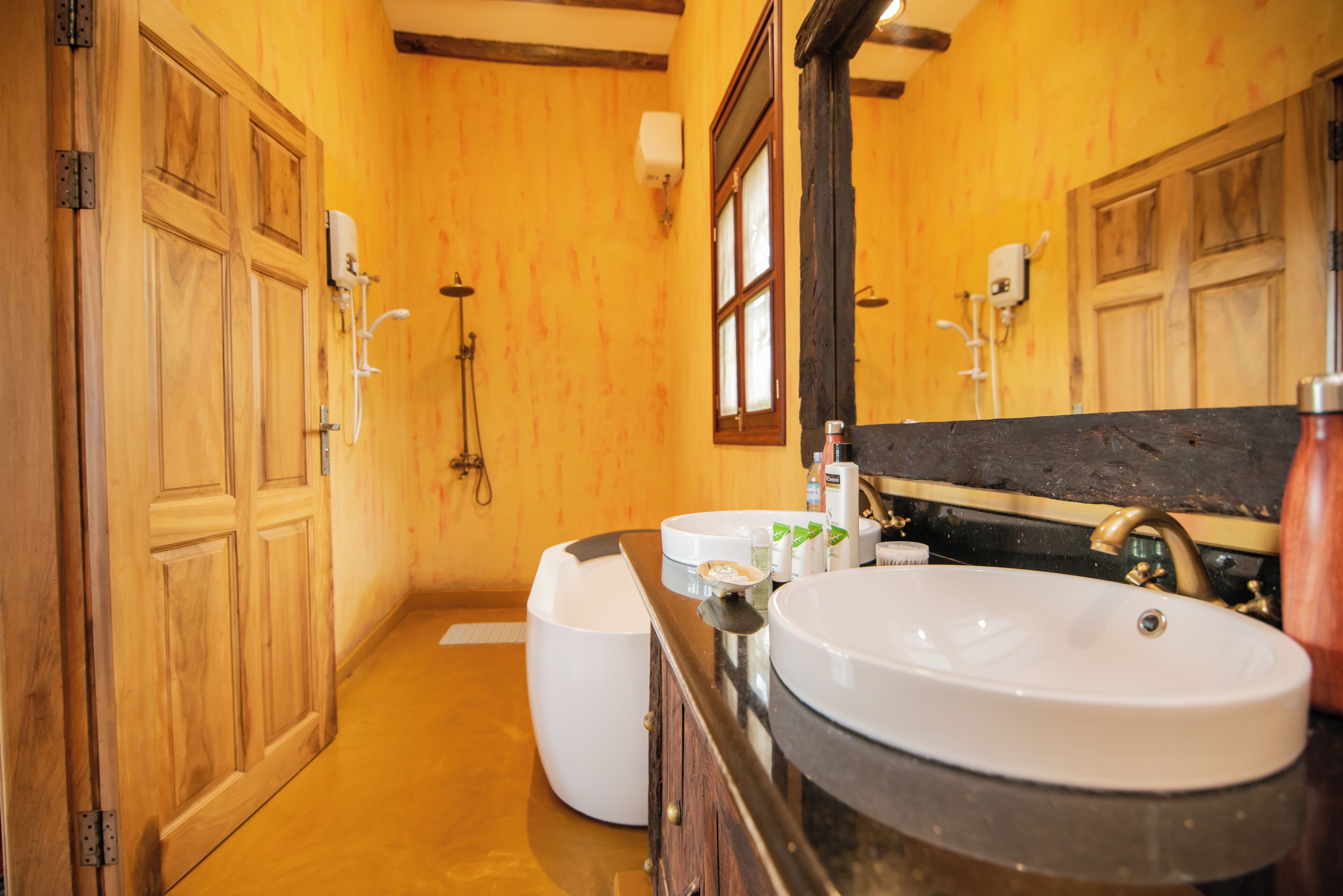 A bathroom with wooden walls, a large mirror, two sinks, and a shower area.