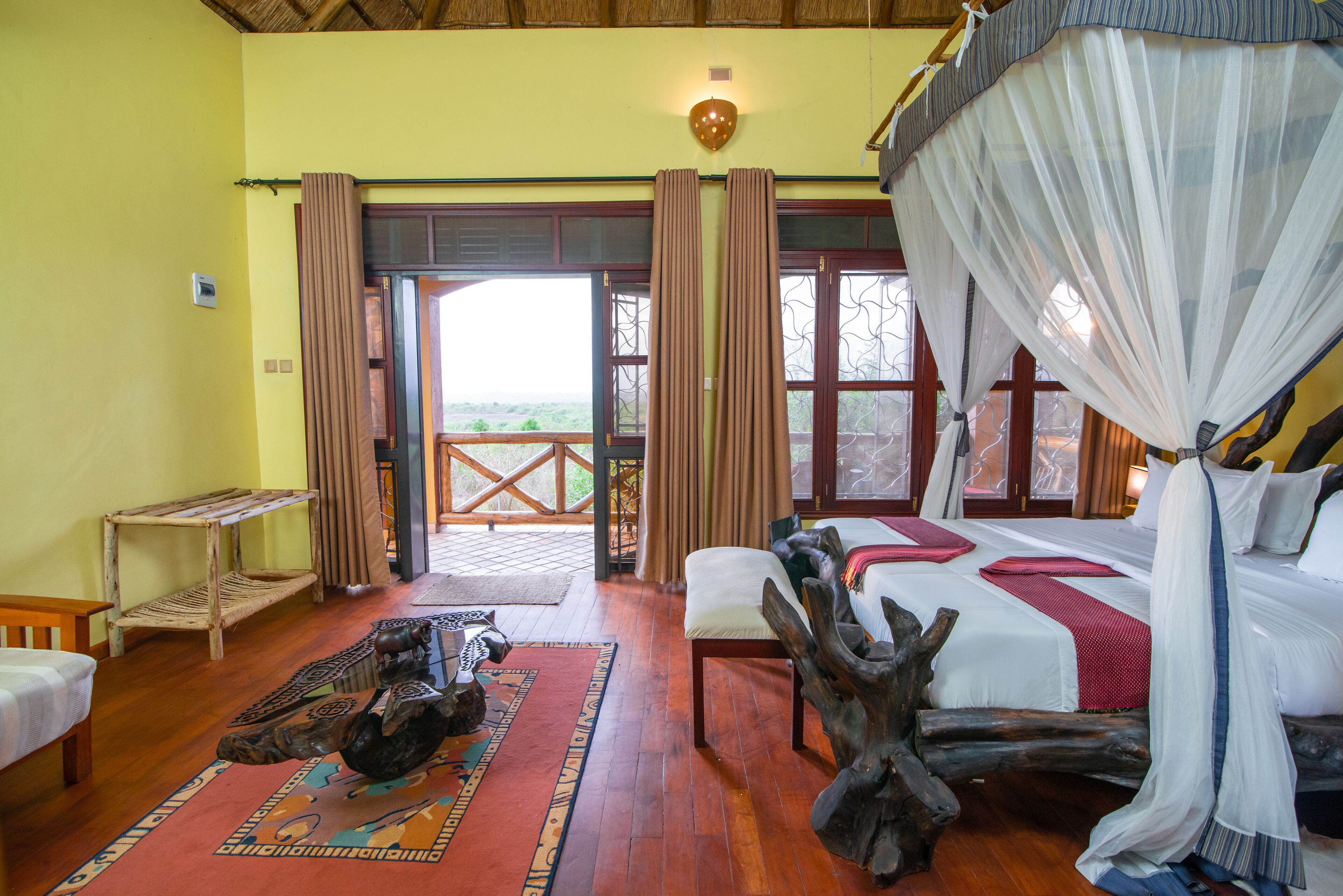 A room with a bed, a bench, a rug, and a wooden sculpture.