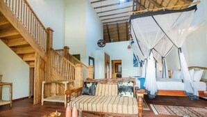 Una habitación amplia con una escalera de madera, una cama con dosel y un sofá con cojines estampados.