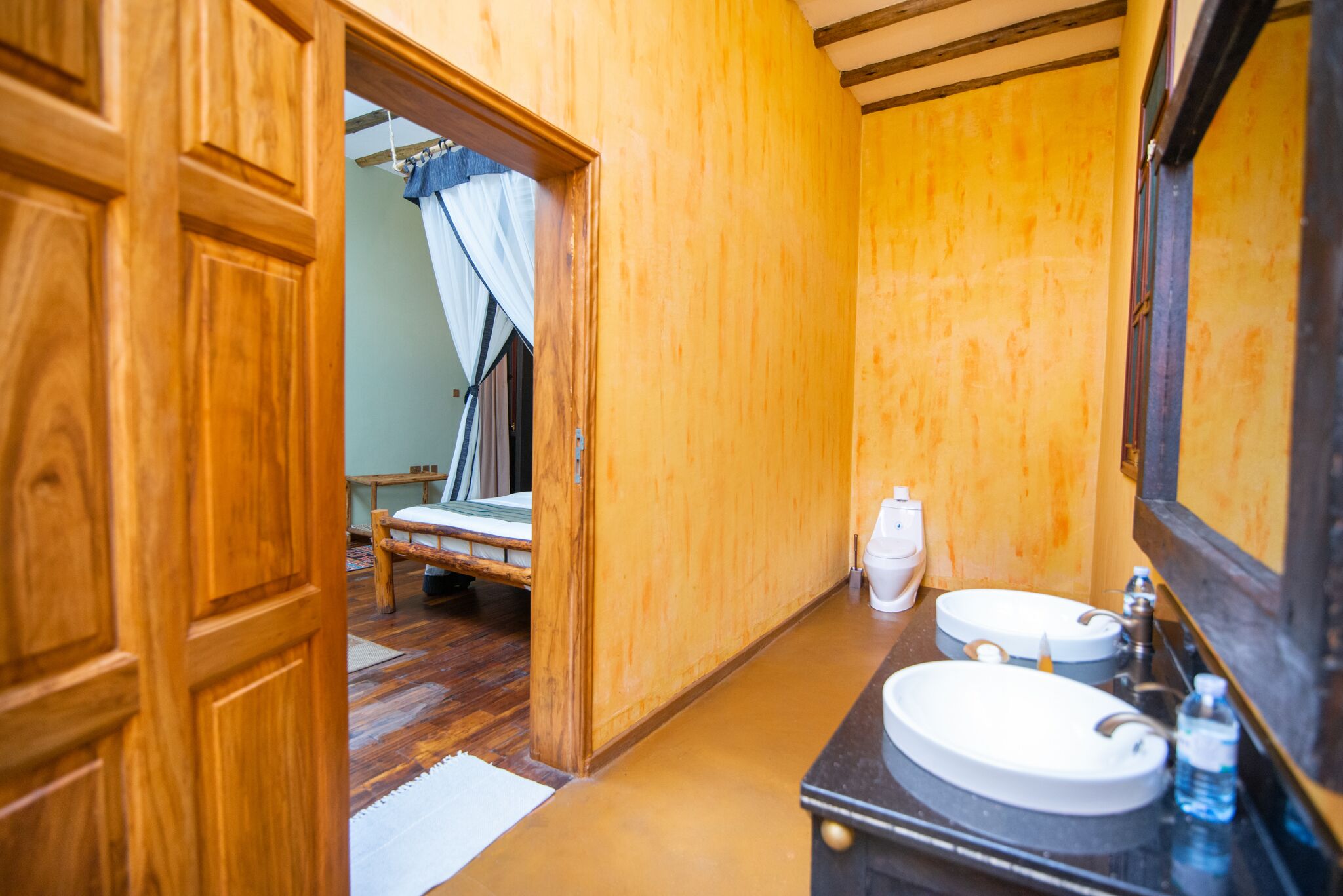 A wooden bathroom with two sinks, a toilet, and a bench.