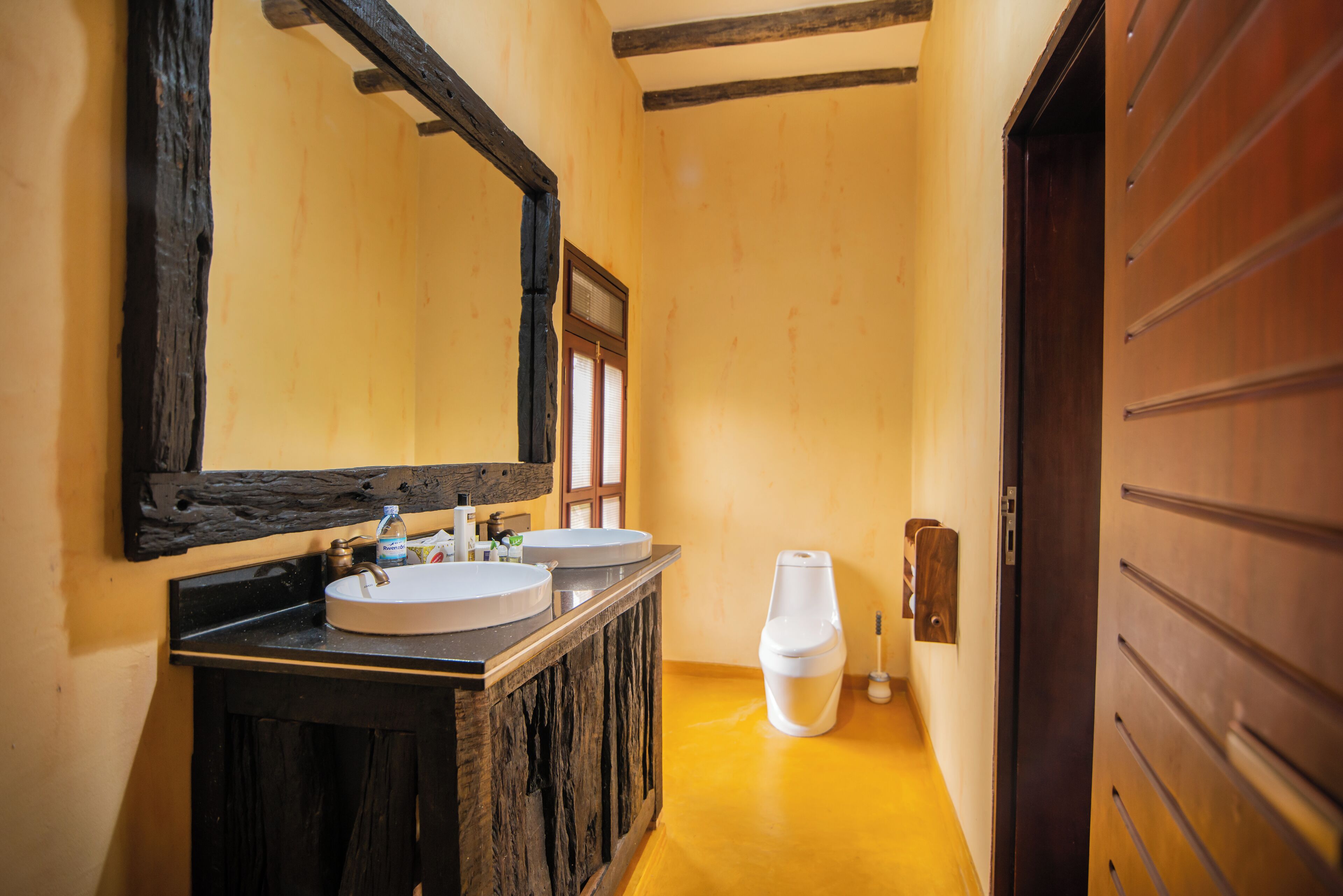 A bathroom with wooden cabinets, two sinks, a large mirror, and a toilet.
