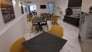 A modern dining area with a black table and yellow chairs, a kitchen with a refrigerator and a coffee machine, and a flat-screen TV on the wall. - Gold Lion Residensea (St. Julian's)