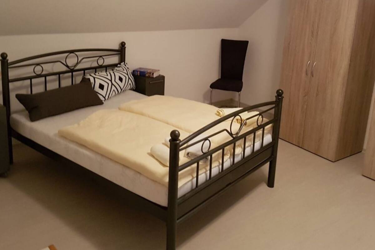 A neatly made bed with a metal frame, a bedside table with a lamp, and a wardrobe.