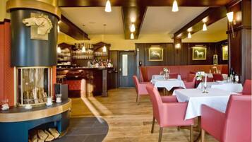 A restaurant with a bar area, wooden flooring, and red upholstered booths.