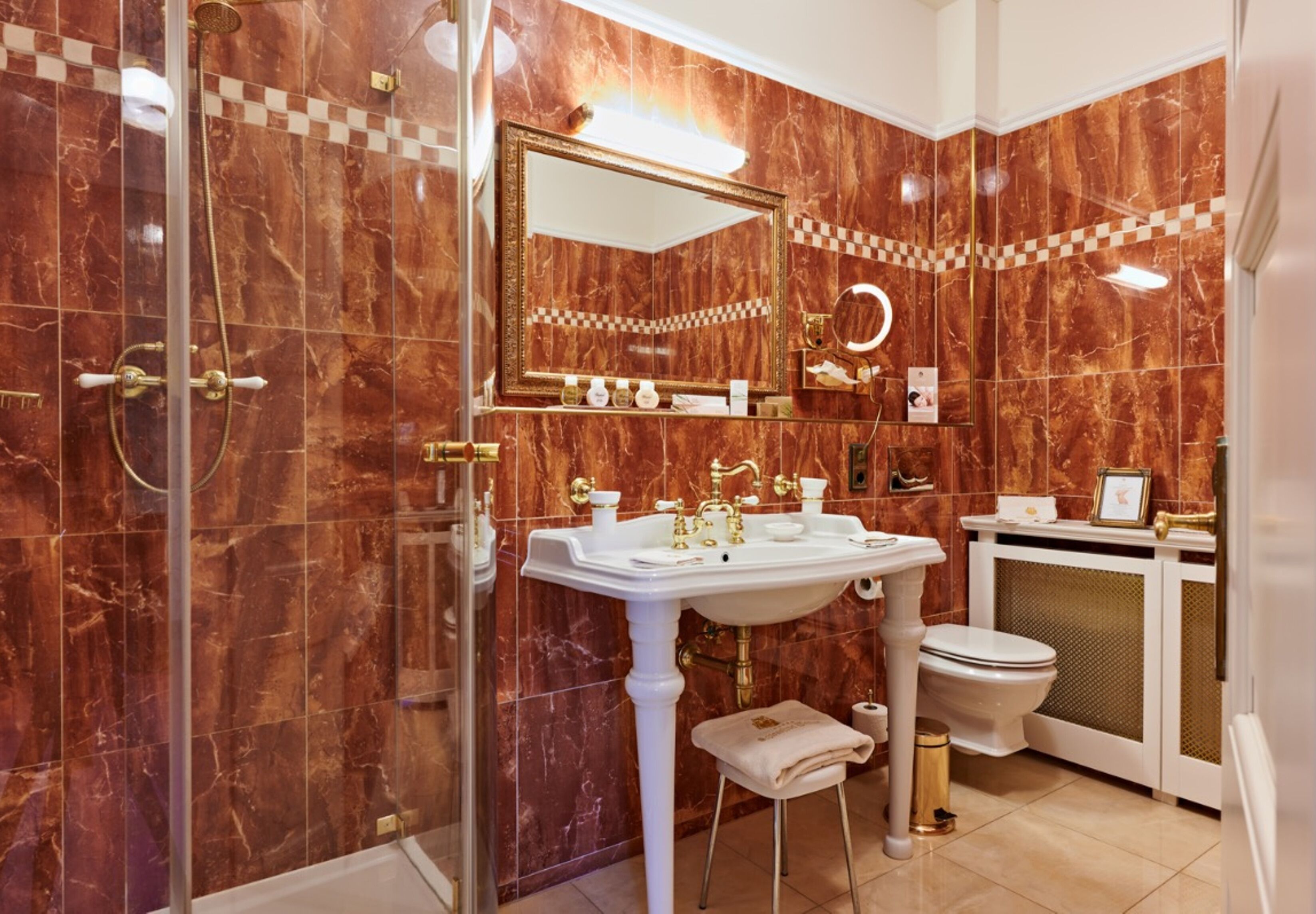 A bathroom with a marble wall, a large mirror, a sink, and a toilet.