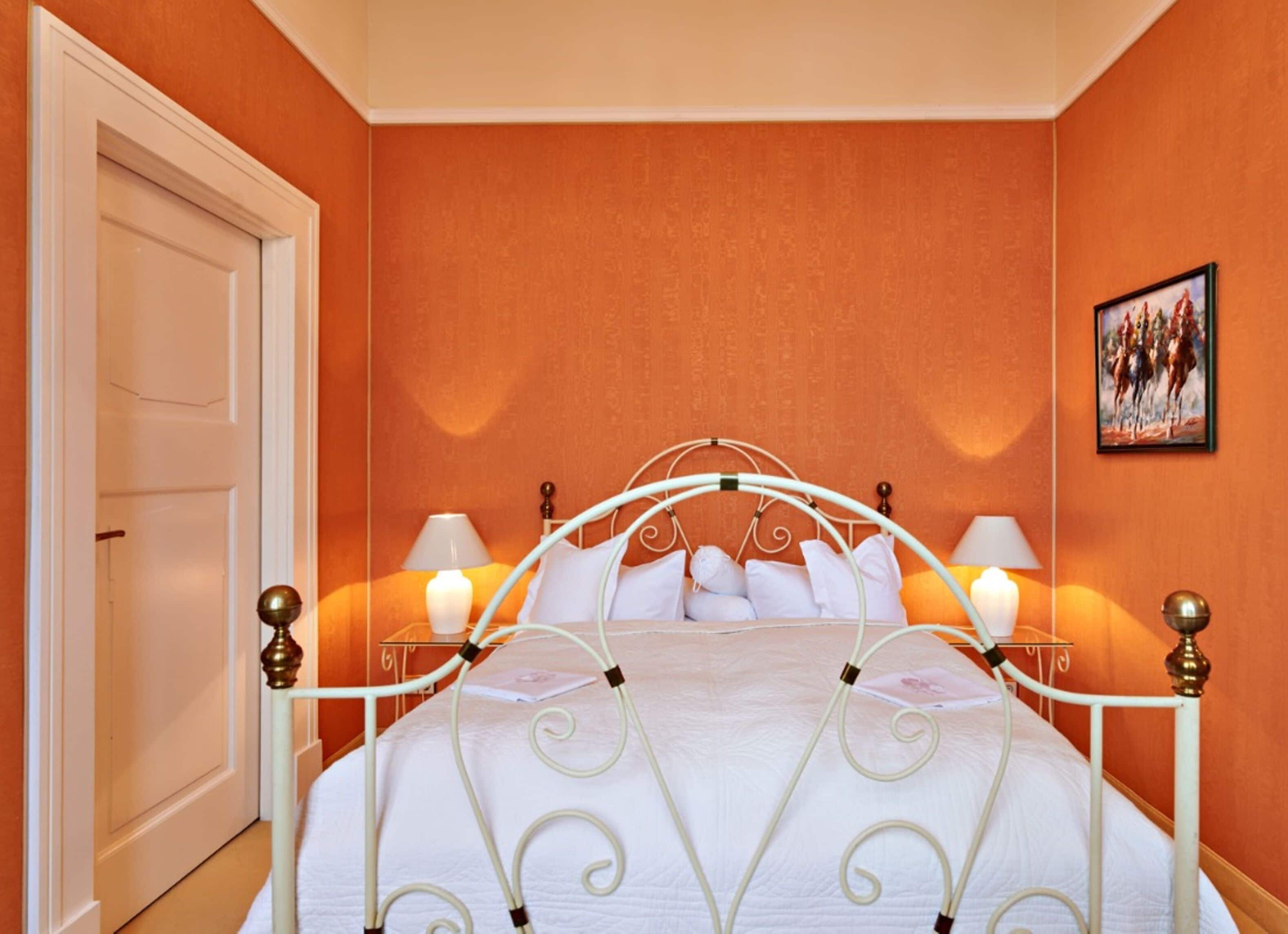 Una habitación de hotel con estructura de cama metálica blanca, ropa de cama blanca y dos lámparas de noche.