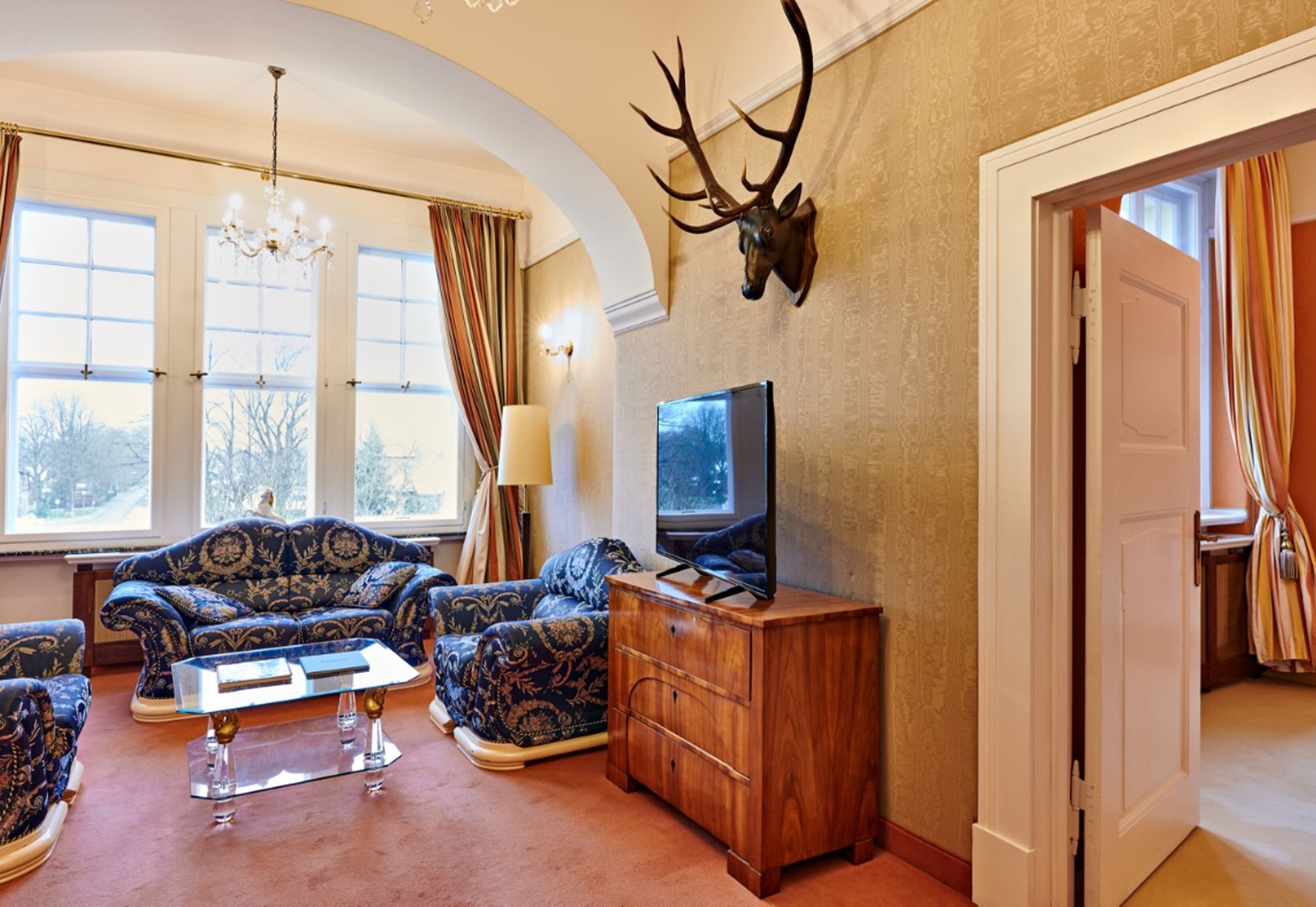 A living room with a sofa set, a wooden cabinet, a mounted deer head, and a television.