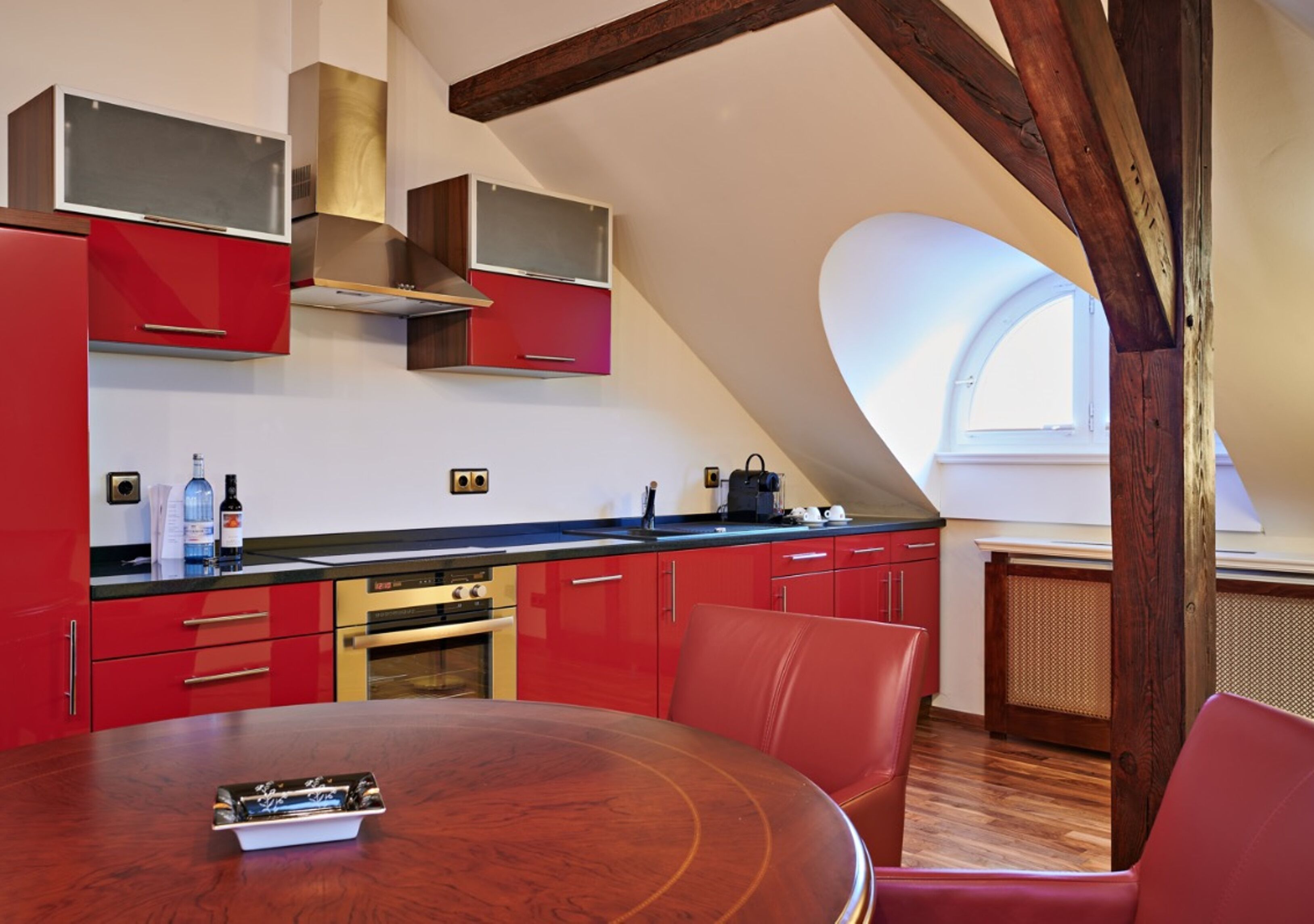 Een moderne keuken met rode kastjes, een houten eettafel en een groot raam.