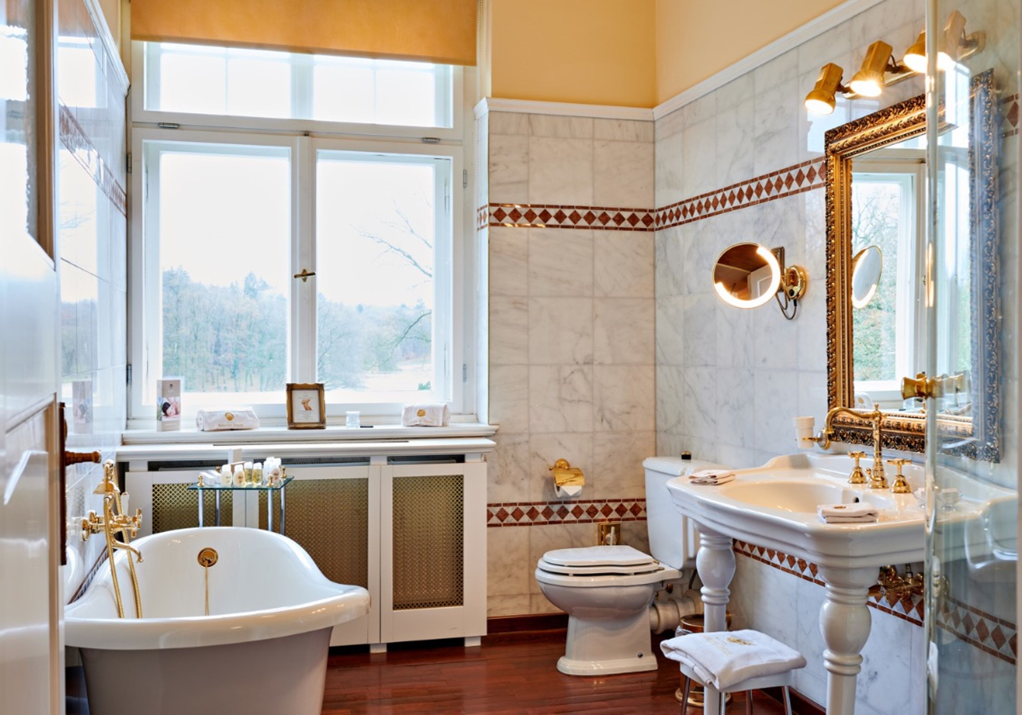 A bathroom with a bathtub, toilet, and sink. There is a window providing natural light, and the walls are tiled with a decorative border.