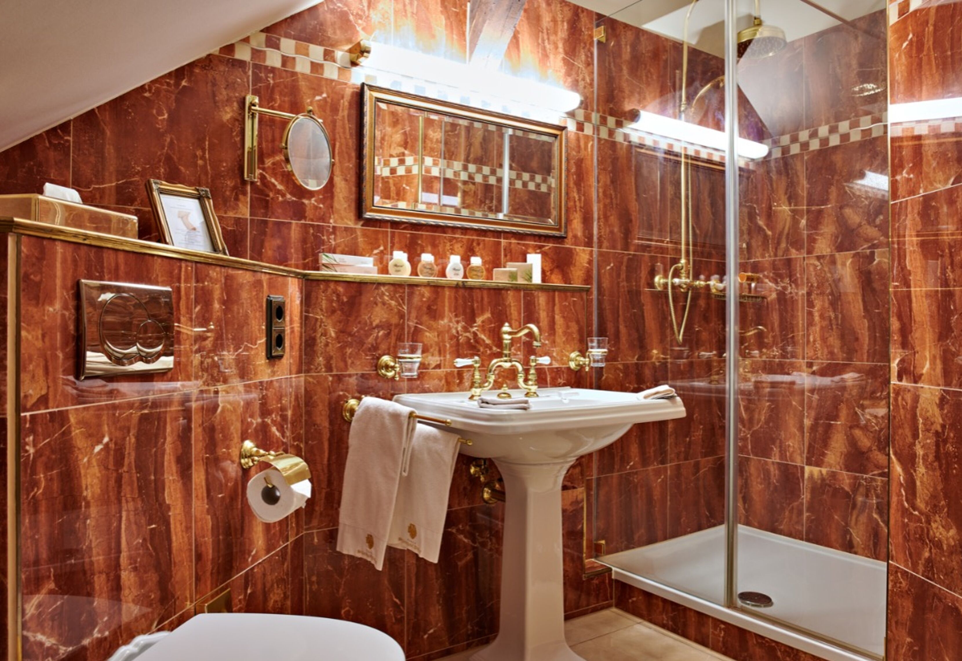 Ein Badezimmer mit Marmorwand, einem Standwaschbecken, einer Glasdusche und einem Waschtisch mit Ablageflächen.