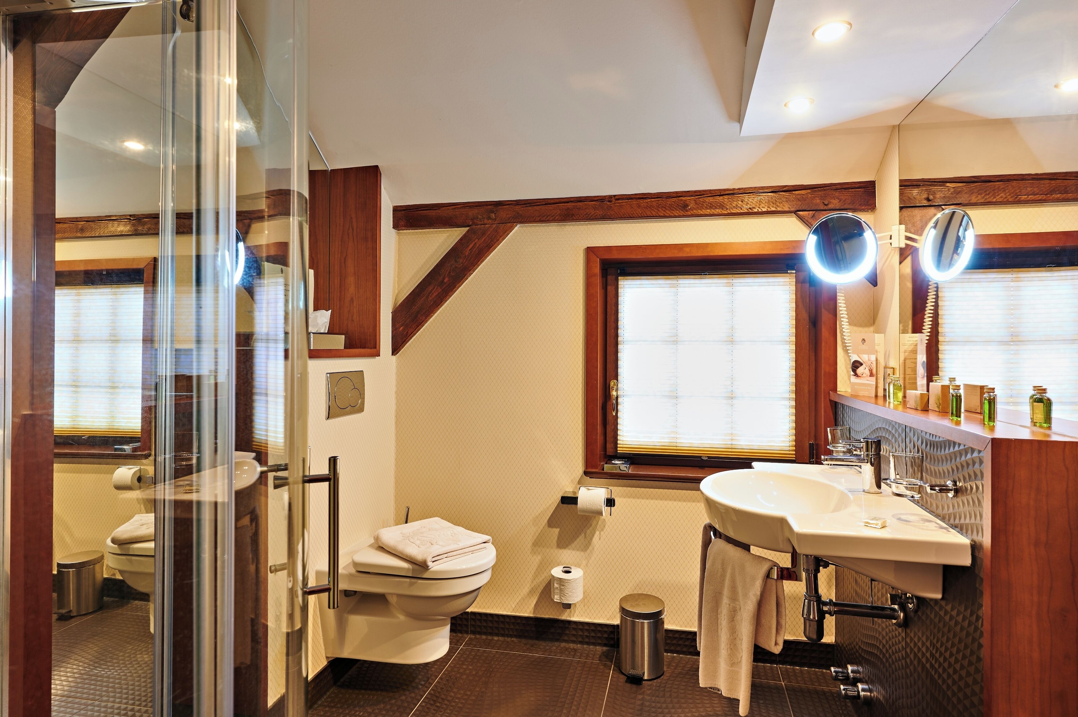 Une salle de bain avec une douche à parois de verre, des toilettes, un lavabo avec un miroir et une fenêtre avec des stores.