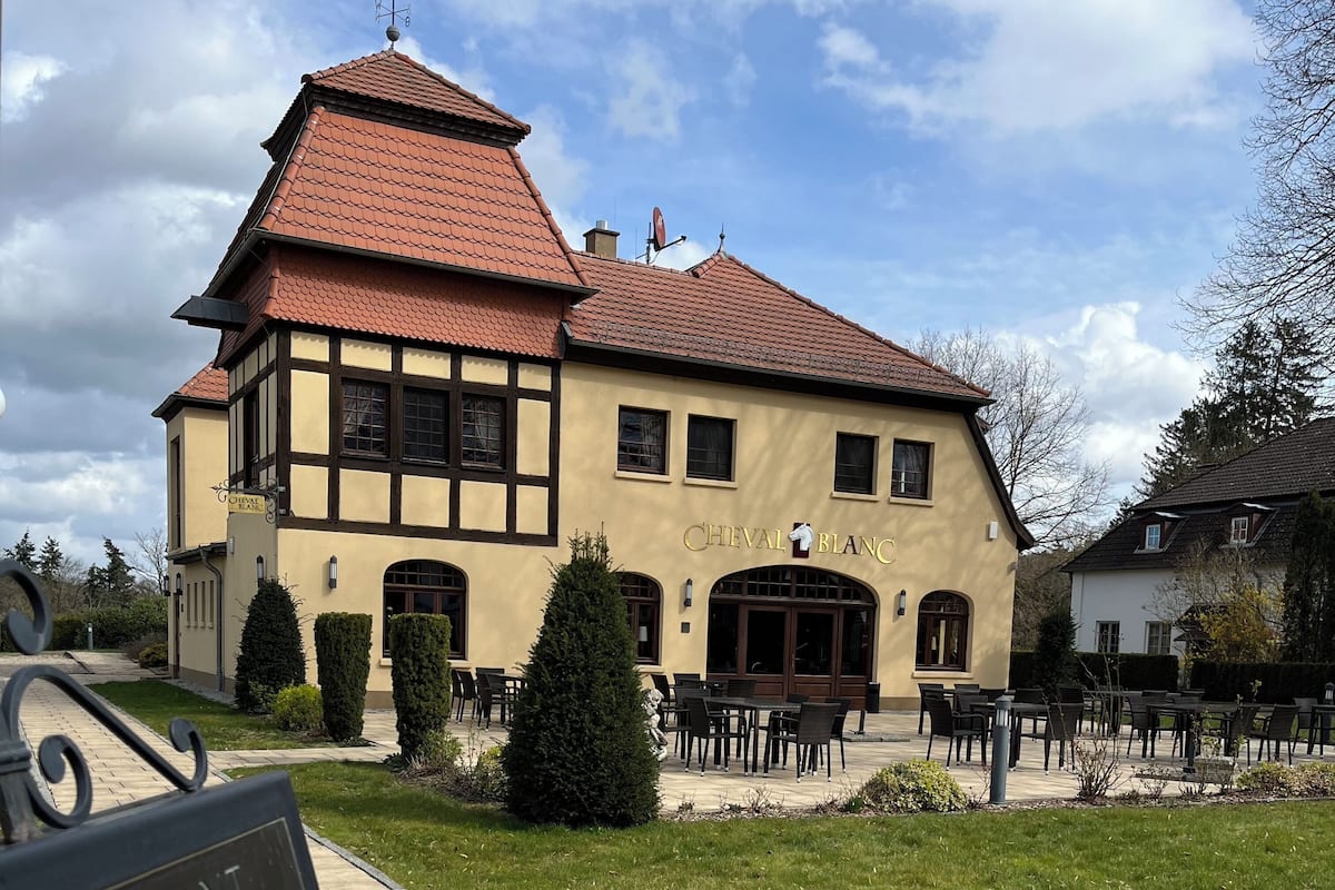 Un bâtiment traditionnel avec une enseigne portant l’inscription « CHEVAL BLANC » et des tables à l’extérieur.