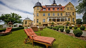 Un grand bâtiment jaune, doté d’un toit recouvert de tuiles rouges, d’une tour et d’une pelouse bien entretenue avec des chaises longues.