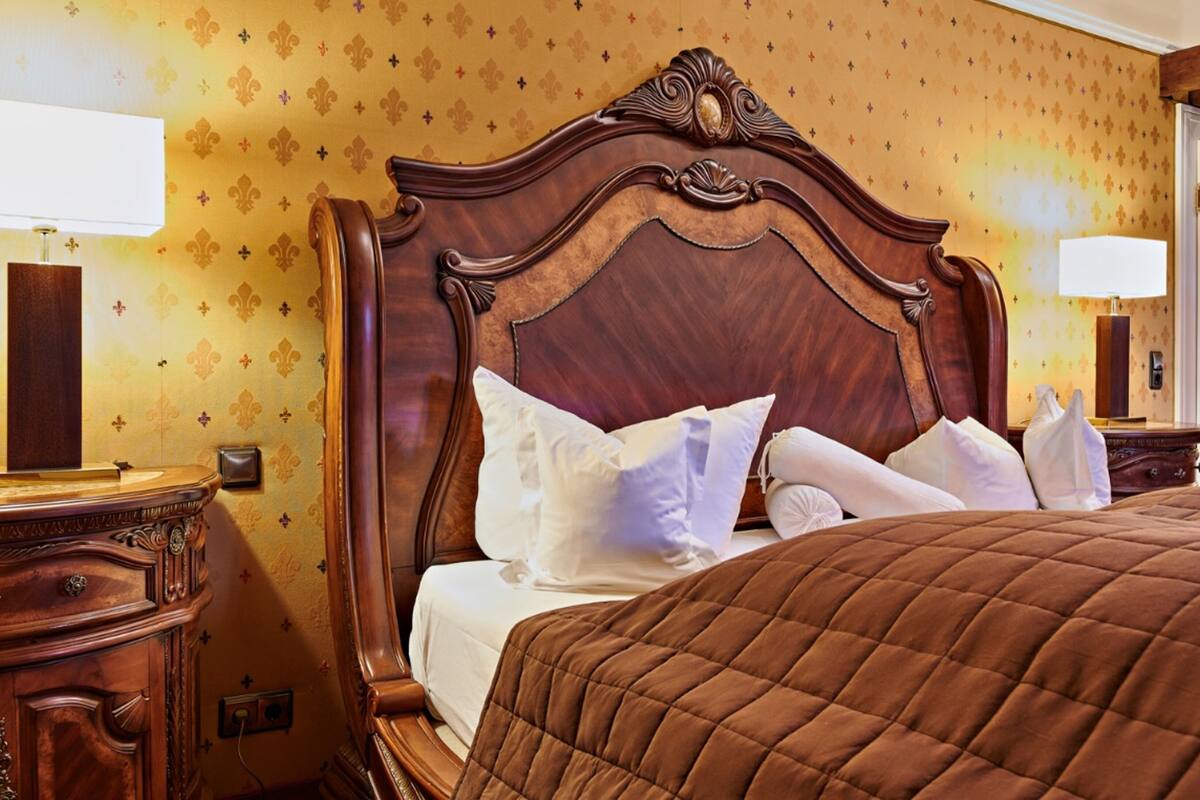 Une chambre d’hôtel avec une grande tête de lit en bois, un lit recouvert de draps blancs et une courtepointe marron matelassée.