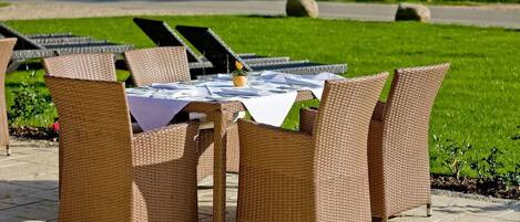 A table set outdoors with wicker chairs, a white tablecloth, and a small potted plant.
