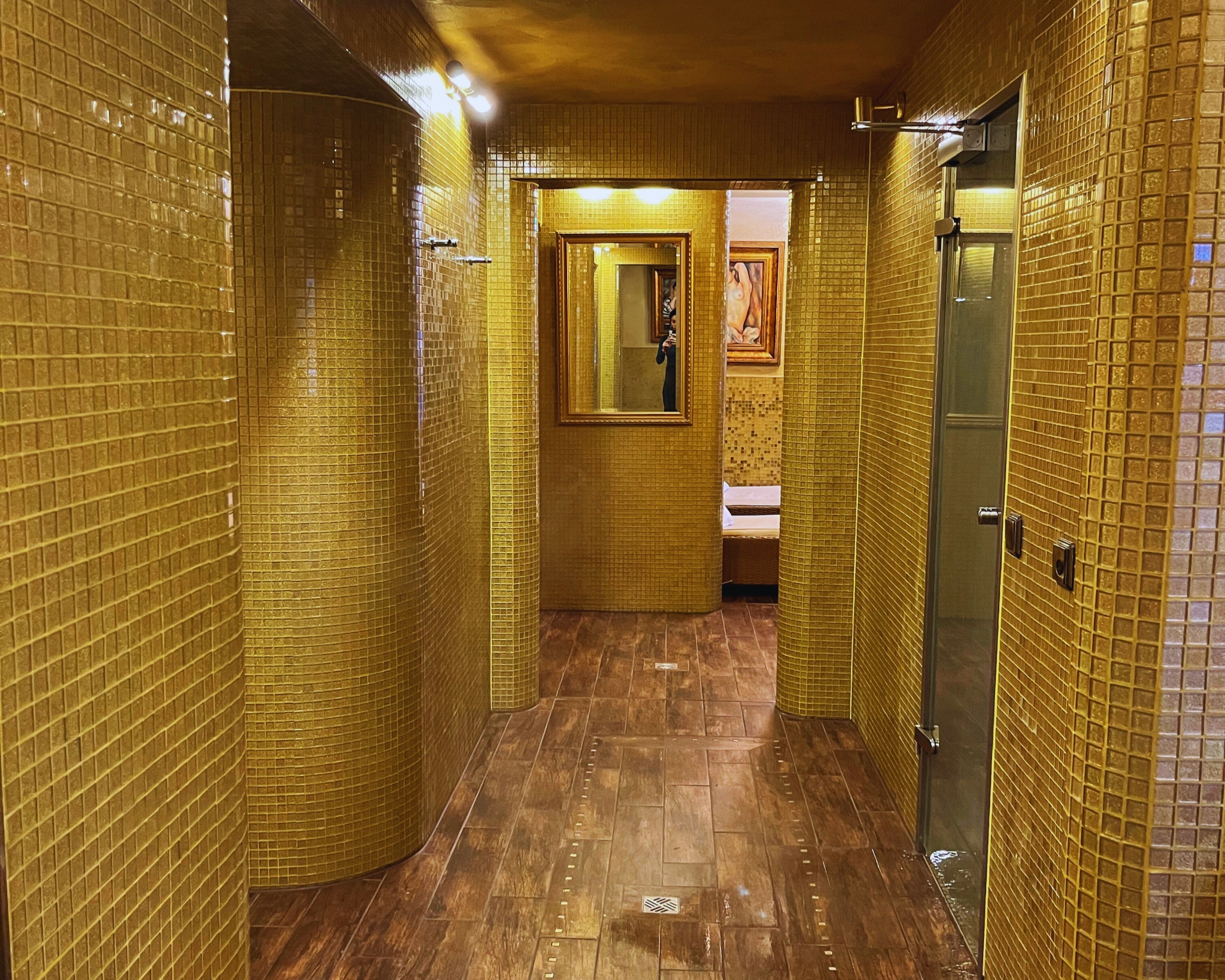 Un pasillo con paredes de azulejos y suelo de madera, que conduce a un baño con un lavabo y un cuadro en la pared.