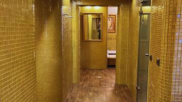 Un pasillo con paredes de azulejos y suelo de madera, que conduce a un baño con un lavabo y un cuadro en la pared.