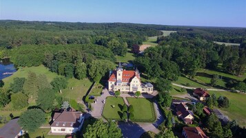 A large, historic building with a central tower, surrounded by well-maintained lawns and a lake.