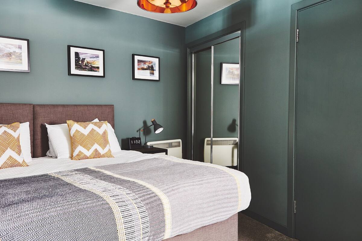 A modern bedroom with a large bed, a bedside table with a lamp, and framed pictures on the wall.