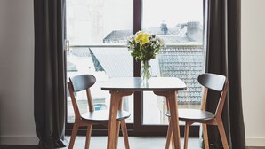 Une pièce avec une table et deux chaises, un vase de fleurs et une vue sur des immeubles par la fenêtre.