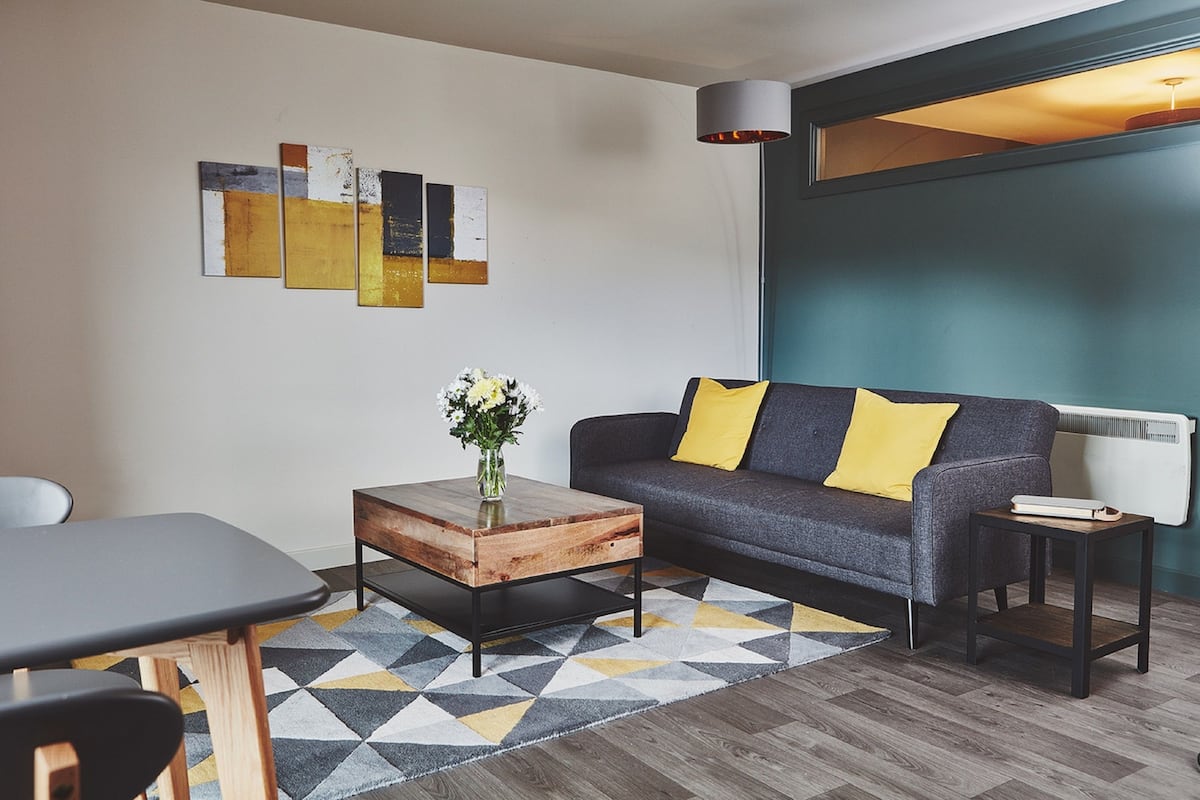 A modern living room with a gray sofa, yellow pillows, a wooden coffee table, and abstract wall art.