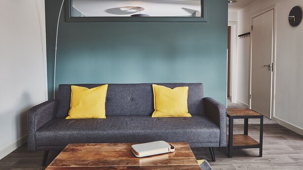 Un salon moderne avec un canapé gris, des coussins jaunes, une table basse en bois et une suspension.